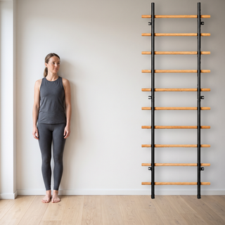 TWHEELS Sprossenwand Standard an der Wand montiert neben einer stehenden Frau, mit sichtbarem Wandabstand und beiden Holmen auf dem Boden.